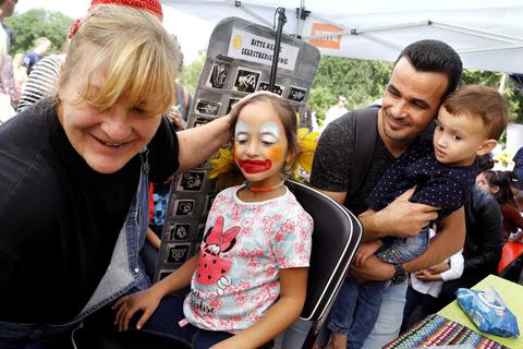 Beim internationalen Kinderspielfest im Prinz-Emil-Garten zaubert Petra Ahlheim (links) Sarah (3) ein Make-up. Vater Mohannad Aydin und Malak (7) schauen zu. Foto: Andreas Kelm  Foto: Andreas Kelm