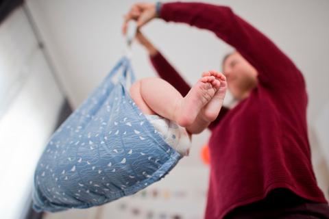Eine Hebamme wiegt im Rahmen der Nachsorge ein Baby (gestellte Szene). 