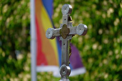 Ein Kreuz der Kirche und dahinter eine Regenbohnenfahne. Im Landkreis Alzey-Worms sind sich die Pfarrer in der Debatte um Segnungen von gleichgeschlechtlichen Paaren einig. Foto: dpa