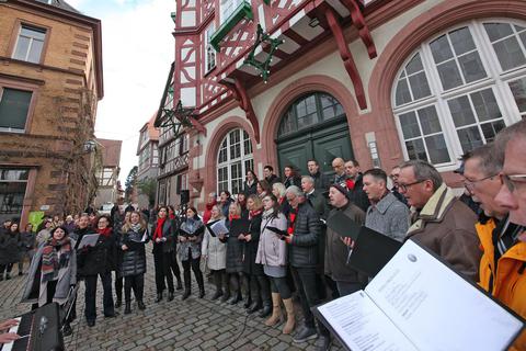 Chordirektor Jürgen Rutz (links) hat 30 Sängerinnen und Sänger vor dem Rathaus versammelt für ein Weihnachtskonzert. © Lutz Igiel