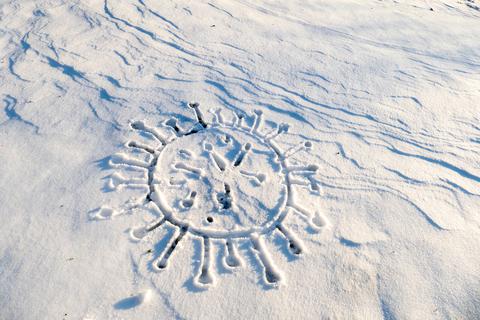 Ein Coronavirus mit Fingern auf eine Schneefläche gezeichnet.