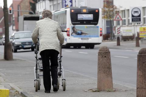 Eine ältere Dame läuft mit einem Rollator einen Gehweg entlang.