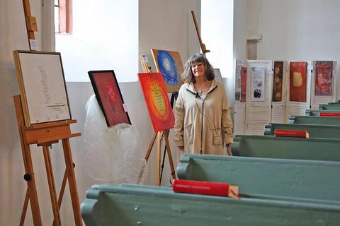 Anette Welp bietet in der Laurentiuskirche „Poesie auf Leinwand“ zum Kauf an. Mit dem Erlös sollen geflüchtete Ukrainer in Trebur unterstützt werden. Foto: Susanne Rapp