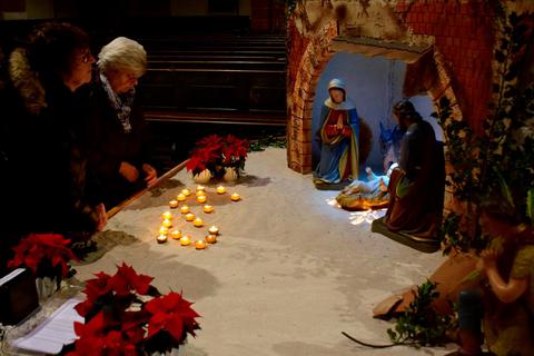 Besucher des internationalen Weihnachtsgottesdienstes entzünden Kerzen und stellen sie vor der Krippe auf. Foto: Lothar Rühl 