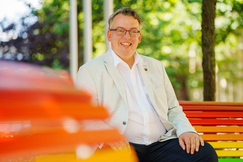 David Profit, Landesbeauftragter für gleichgeschlechtliche Lebensweisen und Geschlechtsidentität in Rheinland-Pfalz, auf einer Bank in Regenbogenfarben. 