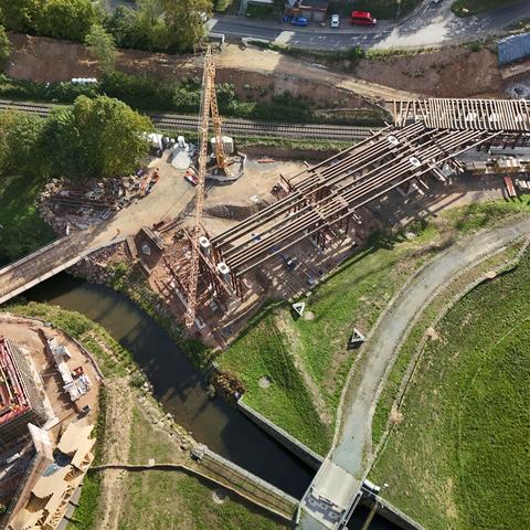 Blick von oben auf die stetig wachsende Zeller Brücke. Links befindet sich das u-förmige Widerlager Nord, das aktuell betoniert wird. Hinter der Mümling sind vier fertig betonierte Pfeiler entstanden. Rechts schließt sich der Bahnübergang und das Widerlager Süd an. 
