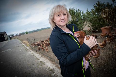 Birgit Biebesheimer mit „Lucky“ auf ihrem Arm. Das Huhn hat als einziges Tier den verheerenden Scheunenbrand in Nordheim (Ruine im Hintergrund) überlebt. Das Huhn lebt jetzt beim Nachbarn, die Familie kämpft indes um ihre Zukunft. Foto: Thorsten Gutschalk