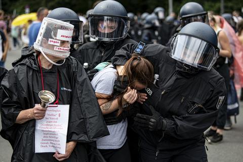 Neben einer Frau, die einen Eimer über den Kopf gestülpt hat, nimmt die Polizei eine Demonstrantin bei einer unangemeldeten Demonstration an der Siegessäule fest. Mehrere Demonstrationen in Berlin waren am Sonntag verboten, darunter eine Kundgebung der Stuttgarter «Querdenken»-Initiative.  Foto: Fabian Sommer/dpa