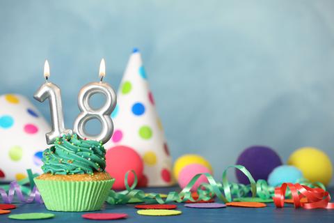 Ein Tisch ist für einen besonderen Geburtstag mit Luftschlangen und Ballons dekoriert - auf einem Muffin mit grünem Zuckerguss brennt die 18 als Kerze.