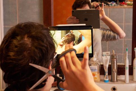 Ein junger Mann schneidet sich nach Anleitung eines Online-Tutorials selber die Haare. Foto: dpa