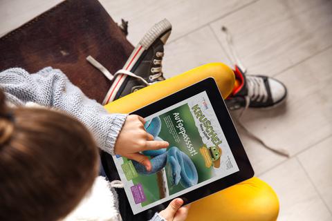 Ein Kind hat ein Tablet auf den Knien und liest die Kinderzeitung "Kruschel" der VRM.