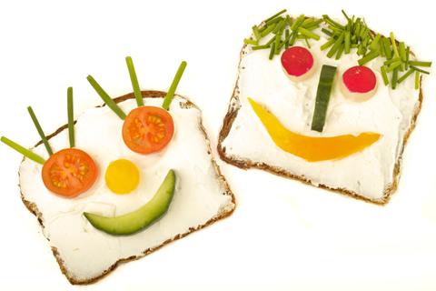 Auf zwei Scheiben Brot sind mit Gemüsestückchen lustige Gesichter gelegt.