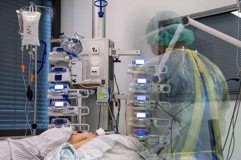 Ein Pfleger steht auf der Corona-Intensivstation neben einem Patienten, der an einem ECMO-Gerät hängt. Foto: Sebastian Gollnow/dpa 