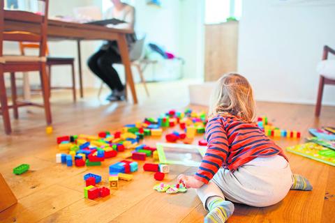 Ein zweijähriges Kind spielt im Wohnzimmer, während seine Mutter Zuhause im Homeoffice an einem Laptop arbeitet. Foto: Julian Stratenschulte/dpa