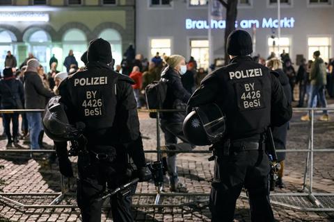 Zwei Polizisten stehen in Schweinfurt vor einer Absperrung, hinter der Corona-Demonstranten vorbeilaufen. Am zweiten Weihnachtsfeiertag wurde hier ein vierjähriges Kind bei einem „Corona-Spaziergang“, der in Gewalt umschlug, leicht verletzt, als die Mutter versucht hatte, eine Polizeiabsperrung zu durchbrechen. Foto: dpa