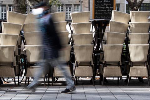 Ein Passant geht an gestapelten Stühlen vorbei, die zu einem Restaurant gehören, das wegen des Coronavirus geschlossen hat.   Foto: Federico Gambarini/dpa