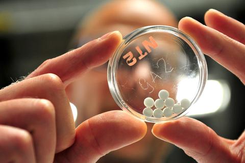 Ein Forscher der Boehringer Ingelheim Deutschland GmbH hält eine Petrischale mit einem fertigen Medikament in Pillenform hoch.  Foto: Jan-Philipp Strobel/dpa